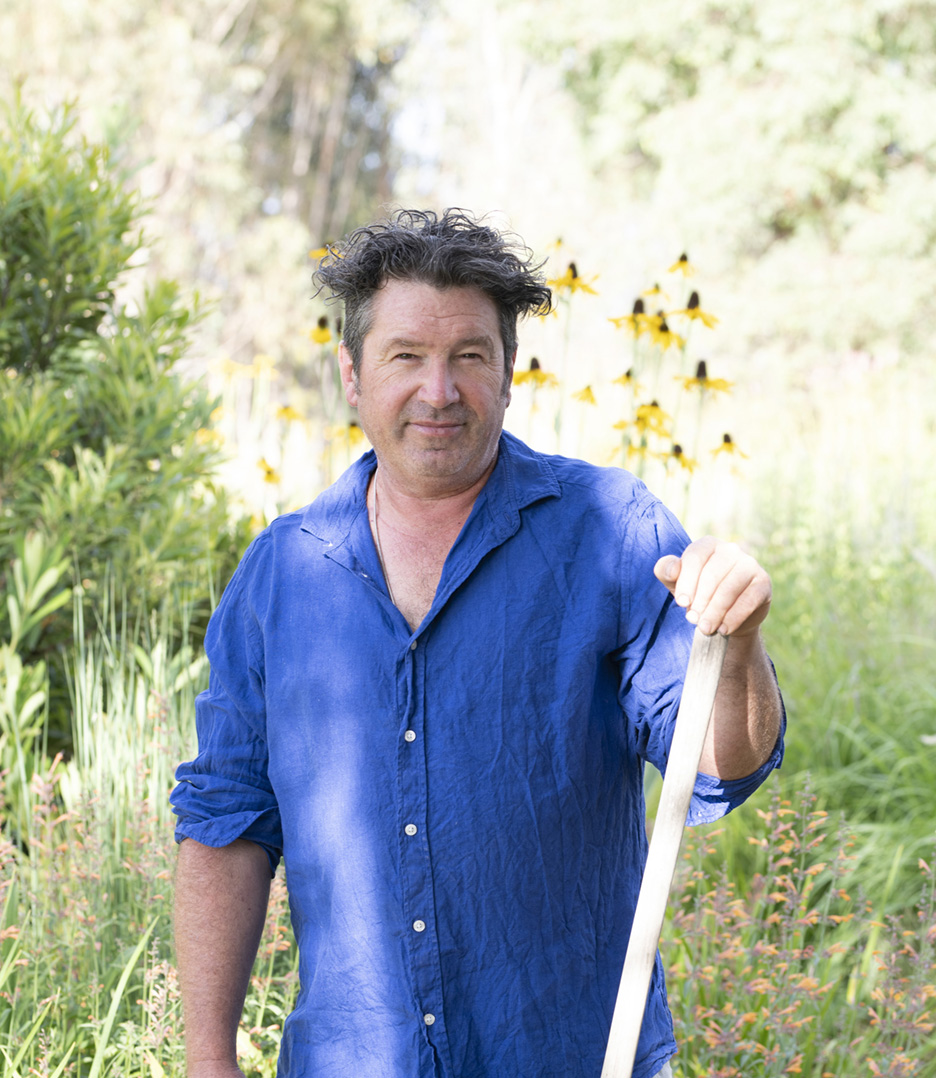 A man in a blue shit hold a shovel in a soft lit garden