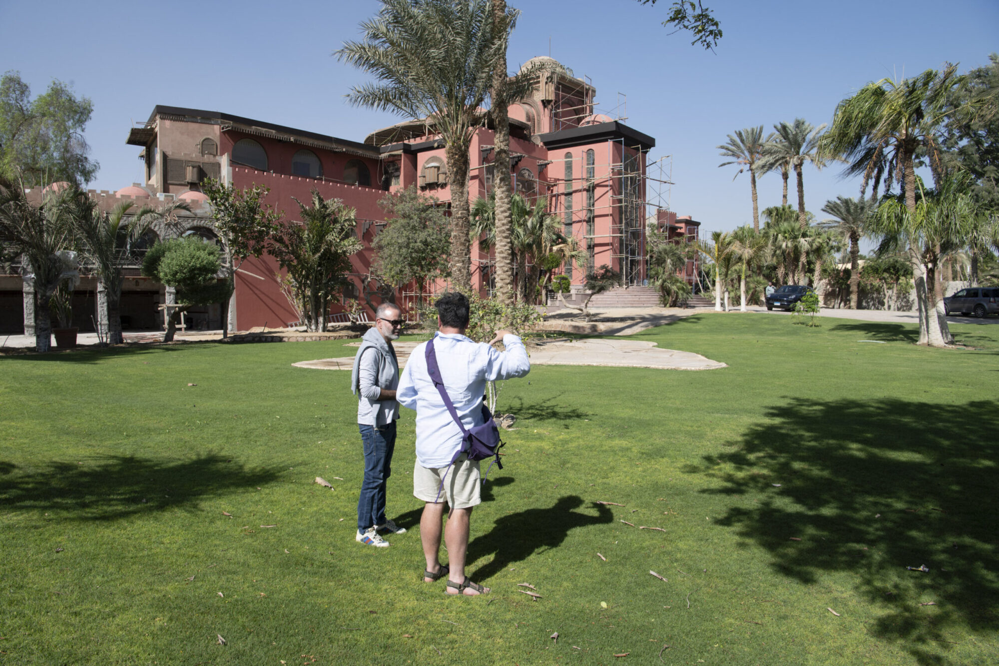 Two men on lawn in front of a large moroccan red house under renovation